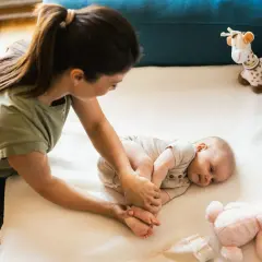Mama delikatnie masuje nóżki niemowlaka, ucząc się, co robić z niemowlakiem. Obok pluszowa żyrafa i króliczek.