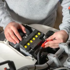 Ręce podłączają kable do akumulatora motocyklowego, szukając odpowiedzi, dlaczego akumulator się rozładowuje.