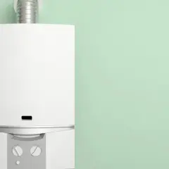 Chaudière basse température blanche, moderne, avec un conduit métallique, installée sur un mur vert pâle.