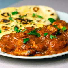 En krämig chicken tikka masala med bitar av kyckling i en smakrik tomatsås, serverad med fluffigt naanbröd.