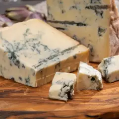 Pezzi di gorgonzola su tagliere di legno, con carciofi e pomodorini. Un assaggio dell'autentica gorgonzola origine.