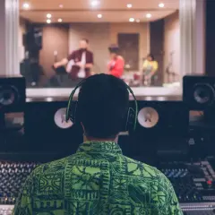 Ingénieur du son aux écouteurs, prêt à ouvrir un studio d'enregistrement, supervise un groupe jouant dans la cabine d'à côté.