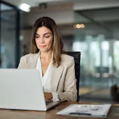 Kobieta w beżowej marynarce pracuje na laptopie. To mały przedsiębiorca, który rozwija swój biznes.