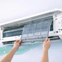 Manos retirando filtro de aire acondicionado split. Limpiar el filtro es clave para cómo eliminar el mal olor del aire acondicionado split y disfrutar de aire fresco.