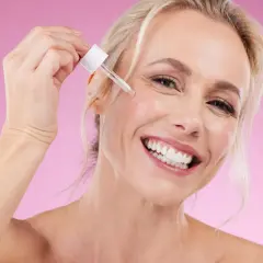 Glad kvinna applicerar serum, oroar sig inte för niacinamide biverkningar.