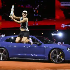 Iga Świątek skacze z pucharem na dachu niebieskiego Porsche, świętując zwycięstwo.