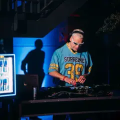 DJ Inox w niebieskiej koszulce z numerem 39 gra muzykę na konsoli DJ-skiej.
