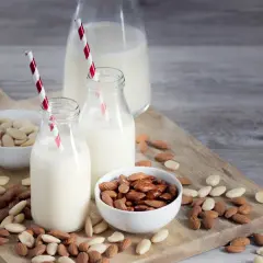 Mleko migdałowe w butelkach z czerwono-białymi słomkami, miseczki z migdałami. Idealne na dieta bez nabiału.