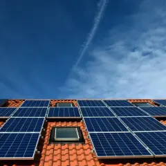 Nowoczesna instalacja PV na dachu z dachówką, pod błękitnym niebem. Panele słoneczne zbierają energię.