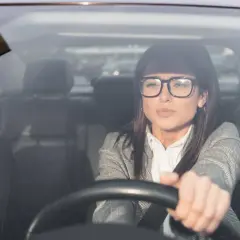 Kobieta w okularach, zamyślona, prowadzi samochód. Jazda w okularach bez wpisu, skupiona na drodze.