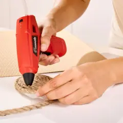 Persona usa pistola de silicona roja para pegar cuerda a cartón. Así es como funciona la pistola de silicona.