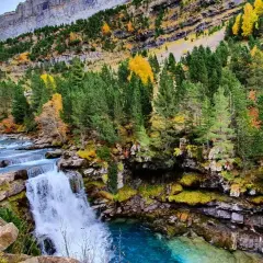 Cascada y río en la ruta Cola de Caballo, rodeados de bosques otoñales y montañas imponentes.