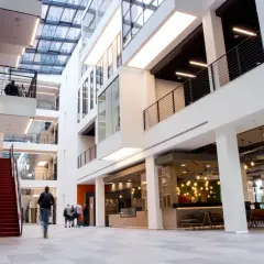 Helles, modernes Gebäude mit Glasdach und roten Treppen. Menschen gehen durch die Lobby des ISM Frankfurt.