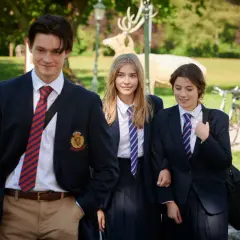 Drei Schüler in Schuluniformen gehen lächelnd durch einen Park. Ein Hirsch-Dekor im Hintergrund erinnert an die **serie gestern waren wir noch kinder**.