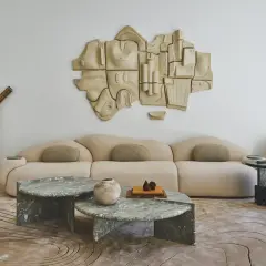 Salon moderne avec canapé beige, tables basses en marbre vert, sculpture murale abstraite et tapis aux motifs organiques. Un endroit parfait pour recevoir une lettre home.