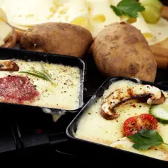 Schmelzender Raclette-Käse mit Salami und Pilzen, dazu Kartoffeln und ein Glas Wein. Perfekt für einen gemütlichen Abend.