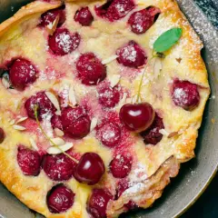 Puszysty omlet z białek z wiśniami i płatkami migdałów, posypany cukrem pudrem. Idealny deser na każdą okazję.