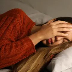 Mujer con suéter naranja se tapa la cara, agotada. Dormir poco engorda y afecta tu bienestar.