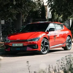 Czerwone Kia EV6 GT, gotowe do sprintu 0-100 km/h, zaparkowane przy ulicy w słoneczny dzień.
