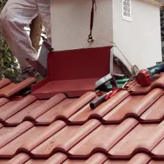 Prace dekarskie przy kominie. Montaż obróbki blacharskiej, która stanowi ważny element opierzenia dachu. Narzędzia i materiały czekają na użycie.