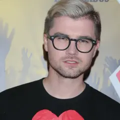 Wujaszek Liestyle w okularach i czarnej koszulce z sercem, na tle tłumu z podniesionymi rękami.
