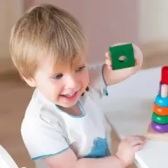 Bambino 3 anni sorridente gioca con blocchi colorati impilati.