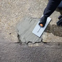 Rękawice i kielnia rozprowadzają zaprawę, wykonując naprawę betonu na zewnątrz.