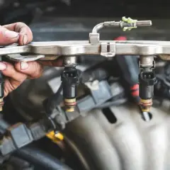 Mano sosteniendo un riel de inyectores de combustible, parte esencial del sistema de inyección directa de un motor.