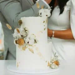 Torta nuziale bianca decorata con fiori secchi e dettagli dorati, perfetta per le canzoni per taglio torta.