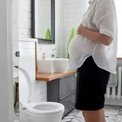 Schwangere Frau im Badezimmer, die sich wegen Durchfall in der Schwangerschaft unwohl fühlt.