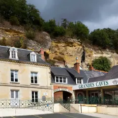 La maison Lacheteau, avec ses façades en pierre et ses toits d'ardoise, se dresse au pied d'une falaise rocheuse.