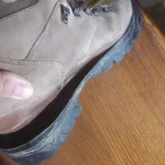 A hand holds a hiking boot where the sole is peeling off, revealing the inside of the shoe.