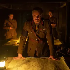 Ein General studiert im Schein einer Lampe eine Karte. Die besetzung von 1917 (film) zeigt ihn mit zwei Offizieren im Hintergrund.