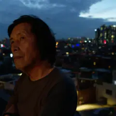 Lee Chang Dong patrzy na nocne miasto z balkonu.