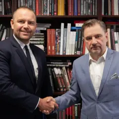 Dwóch mężczyzn w garniturach ściska sobie dłonie na tle regałów z książkami. Czy wybór Karola Nawrockiego na kandydata był konsultowany z Andrzejem Dudą?