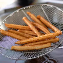 Churros co to? Złociste, chrupiące paluszki smażone na głębokim oleju, wyciągane właśnie na sicie.