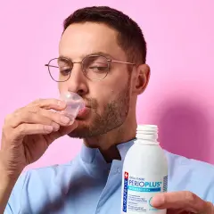 Uomo con occhiali beve collutorio da un bicchierino. Il flacone di Curasept gel va risciacquato.