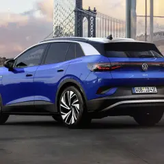 Niebieski VW ID.4 z imponującym zasięgiem, zaparkowany na tle miejskiego krajobrazu z mostem w tle.