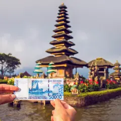 Ręka trzyma banknot 50 000 rupii indonezyjskich na tle świątyni na wodzie na Bali.