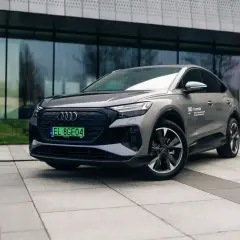 Szary Audi Q4 elektryk z zieloną tablicą rejestracyjną stoi przed nowoczesnym budynkiem.