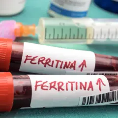 Dwie probówki z krwią oznaczone "Ferritina" i strzałką w górę, sugerujące potrzebę podniesienia poziomu ferrytyny. W tle strzykawka i inne materiały medyczne.
