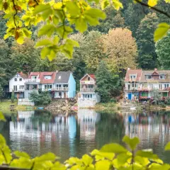 Domki nad jeziorem w jesiennej scenerii, odbijające się w wodzie.