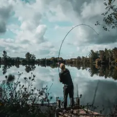 Wędkarz łowi na ciężki spinning z opadu w głębokich rynnach odrzańskich. Wędka wygięta w łuk, woda spokojna, odbija chmury.