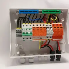 Wnętrze białej obudowy, gdzie trwa budowa rozdzielni elektrycznej. Widoczne bezpieczniki, wyłączniki i zabezpieczenia przeciwprzepięciowe.