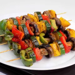 Kolorowe szaszłyki warzywne z grillowanymi paprykami, cukinią i pieczarkami, ułożone na białym talerzu.