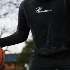 Mężczyzna w czarnej bluzie koszykarskiej z logo "Meadour" trzyma piłkę do koszykówki.