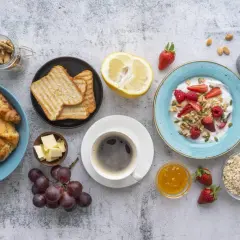 Un tavolo pieno di idee su cosa mangiare a colazione: croissant, toast, yogurt con frutta, caffè, uva e cereali.