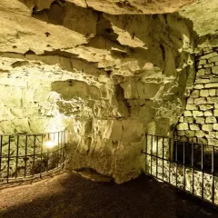 Intérieur des boves d'Arras, un réseau de galeries souterraines aux murs de pierre brute et de briques, éclairées par une lumière jaune.
