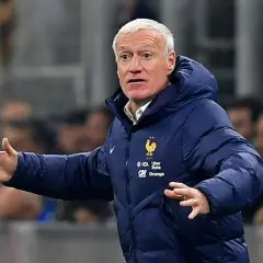 Didier Deschamps, trener Francji, w niebieskiej kurtce z herbem reprezentacji, gestykuluje na boisku.