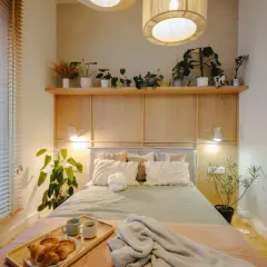Drewniana ściana za łóżkiem z półką pełną roślin i lampkami. Inspiracje do sypialni z naturalnymi akcentami.